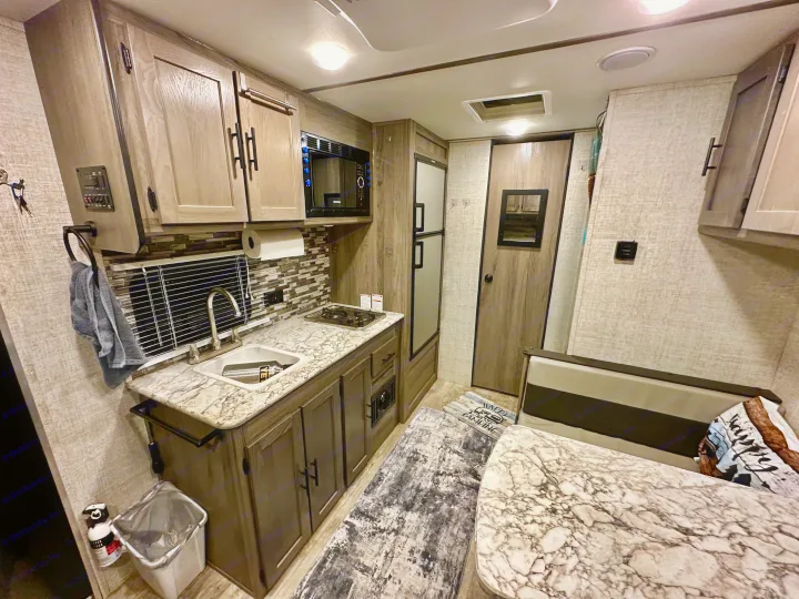 This modern RV rental features a compact kitchen with sink, microwave, stove, and a dinette area with built-in seating.. Gulf Stream Ameri-Lite Super Lite 2021