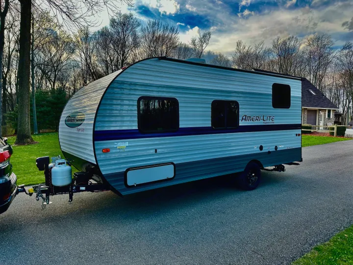 Gray/blue Ameri-Lite travel trailer, perfect for an RV rental, parked on a driveway. Bare trees & a house in the background.. Gulf Stream Ameri-Lite Super Lite 2021