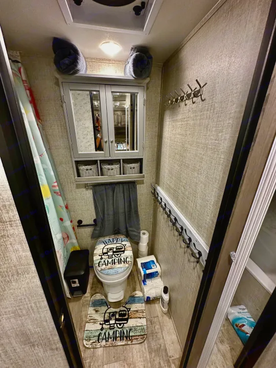 Inside a compact RV rental bathroom, featuring camping-themed decor, toilet, shower curtain & storage.. Gulf Stream Ameri-Lite Super Lite 2021
