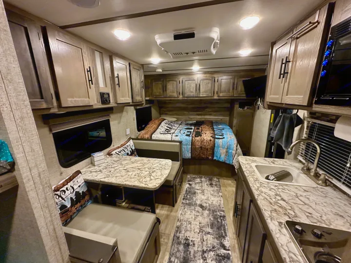 Cozy RV rental interior showcasing a bedroom, dinette, and kitchen area with overhead cabinets, ideal for road trips.. Gulf Stream Ameri-Lite Super Lite 2021