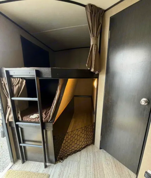 Cozy RV rental interior with bunk beds, ladder, curtains, and safety net, perfect for family sleeping space.. Grand Design Imagine 2018