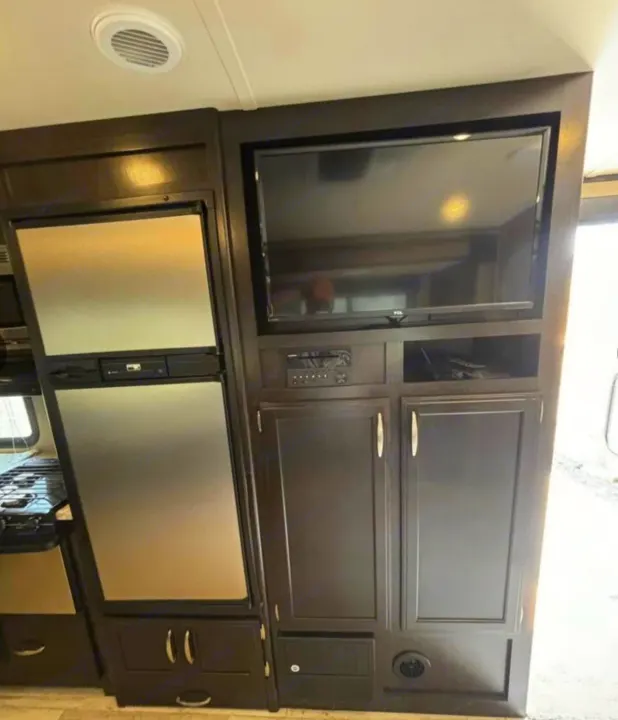 This RV rental interior features a compact kitchen with a refrigerator and an entertainment area with TV & cabinets.. Grand Design Imagine 2018