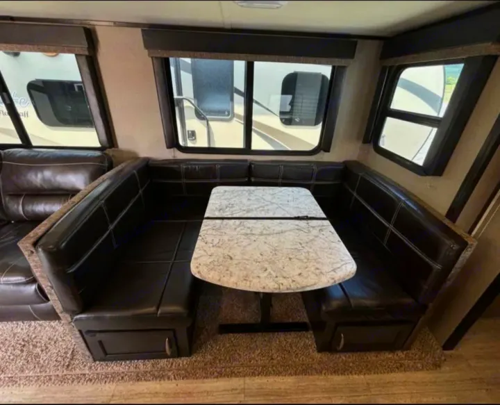 RV rental's U-shaped dinette: dark, comfortable seating with a light speckled table in a well-lit RV interior.. Grand Design Imagine 2018