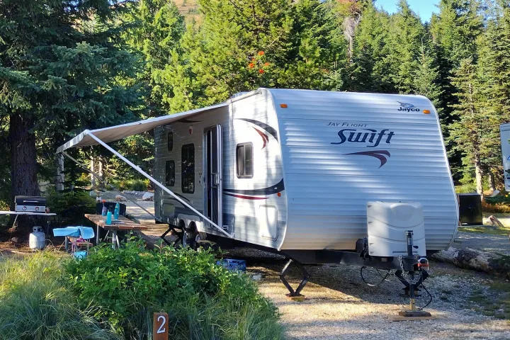 Jayco Swift travel trailer at a forested campsite, perfect for an RV rental getaway. Awning extended, ready for outdoor living.. Jayco Jay Flight Swift 2011