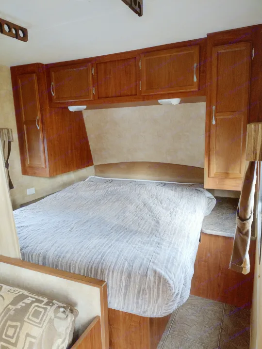 Comfortable RV rental bedroom featuring a large bed, overhead wood cabinets, and built-in lights for cozy travel.. Jayco Jay Flight Swift 2011