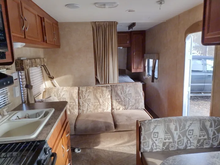 RV rental interior: A compact living space with kitchen counter, overhead cabinets, patterned sofa, and a bedroom area.. Jayco Jay Flight Swift 2011