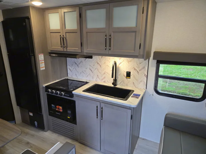 This RV rental's kitchen features modern light wood cabinets, black appliances (fridge, stove, sink), and a stylish backsplash.. Keystone Hideout 240BH 2025