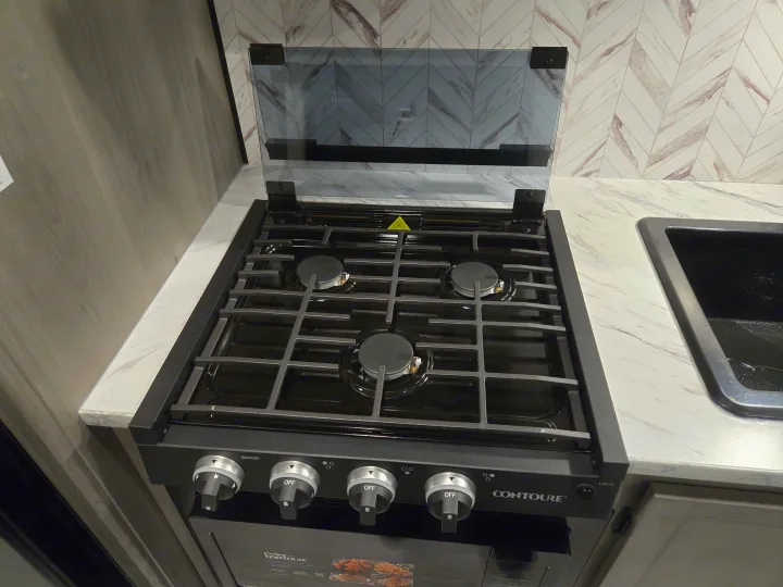 Modern RV rental kitchen featuring a black 3-burner gas cooktop with an open glass cover, on sleek marble-look countertops.. Keystone Hideout 240BH 2025