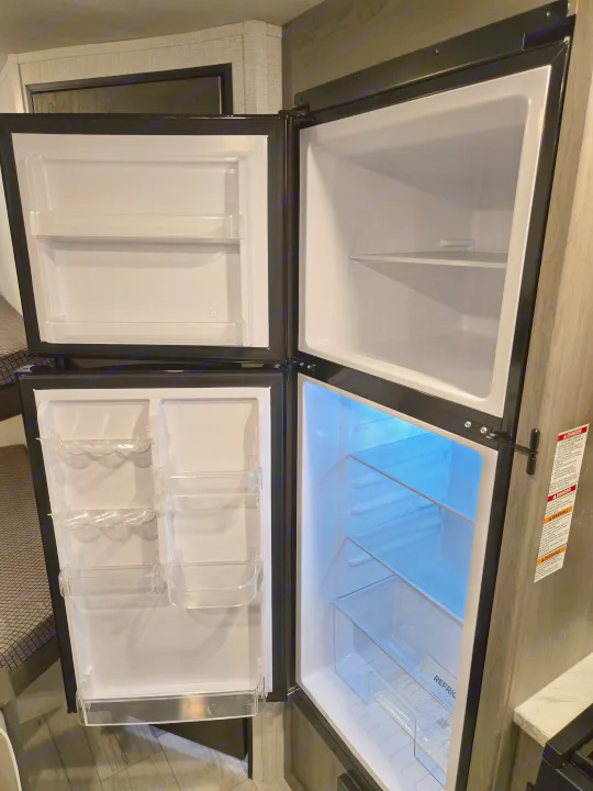 New RV rental kitchen features a clean, empty refrigerator and top freezer, perfect for your adventure.. Keystone Hideout 240BH 2025