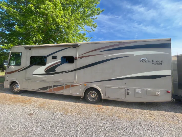 A Coachmen Pursuit RV rental parked on gravel under a blue sky with trees. Ideal for your next motorhome adventure.. Forest River Coachmen Pursuit 2017