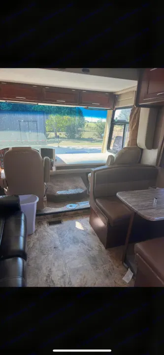 RV rental interior showcasing the driver's area, dinette, and overhead cabinets, with a bright view through the front windshield.. Forest River Coachmen Pursuit 2017