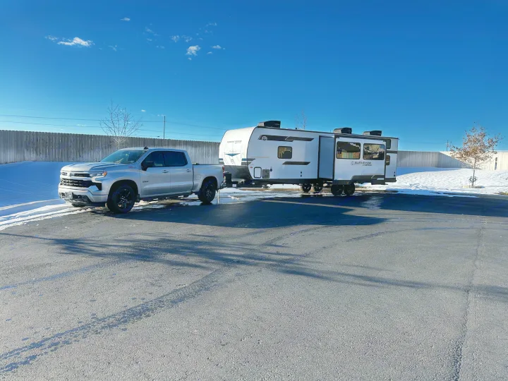 Silver pickup truck towing a white Forest River RV on asphalt next to snow, ideal for your next rv rental adventure.. Forest River Surveyor Legend X 2025