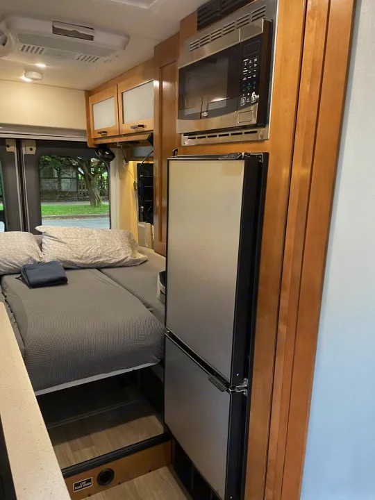 Cozy RV rental interior with bed, built-in microwave, and refrigerator. Functional camper van living space.. Coachmen Beyond 22D 2020