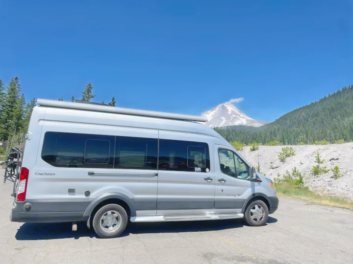 Silver Coachmen Beyond RV rental van facing a majestic snow-capped mountain, lush forest, and clear blue sky.. Coachmen Beyond 22D 2020