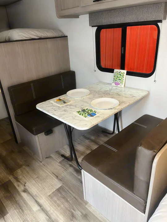 Enjoy an RV rental! This cozy dinette area features bench seating, a marble-look table, and a nearby bunk bed.. Dutchmen Coleman Lantern LT 17B 2024