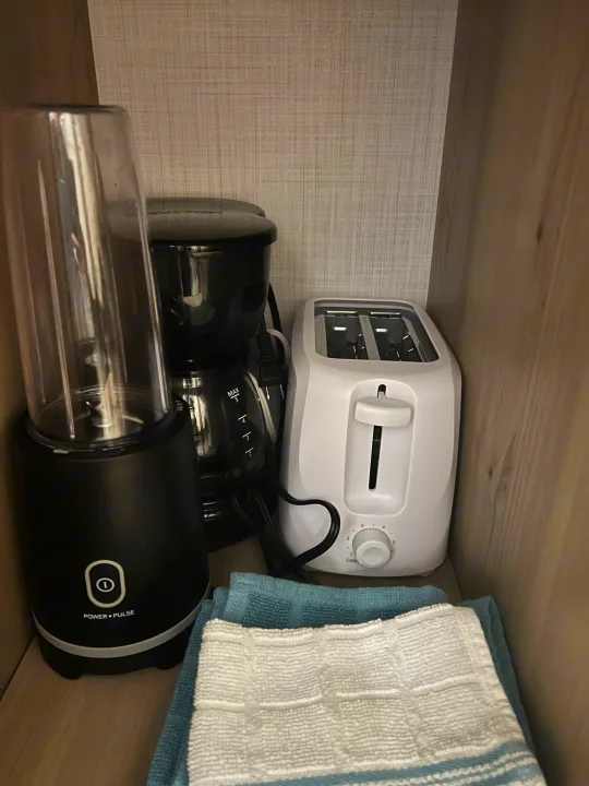 RV rental kitchen essentials: a black blender, coffee maker, white toaster, and folded towels in a compact cabinet.. Forest River Rockwood Geo Pro 2024