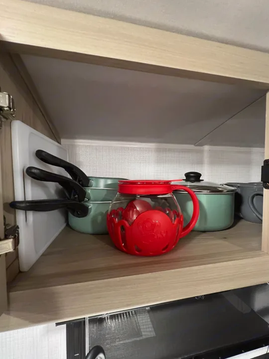 RV rental kitchen: Neatly stored green cookware, a cutting board, and a red pitcher inside a cabinet.. Forest River Rockwood Geo Pro 2024
