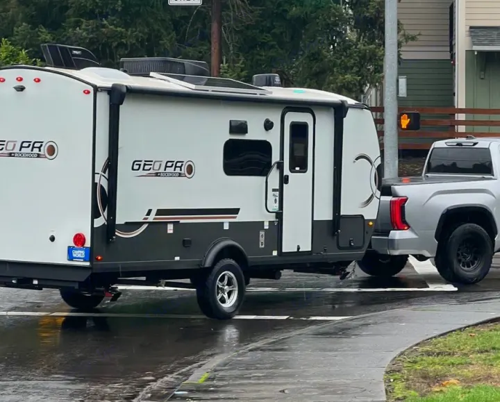 A grey pickup truck tows a Geo Pro travel trailer, perfect for an RV rental road trip on a wet day.. Forest River Rockwood Geo Pro 2024
