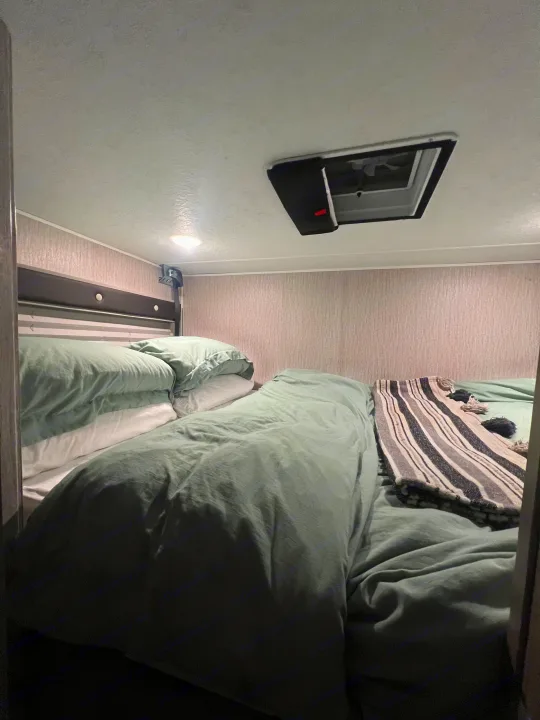 Cozy RV rental bedroom with two bunks, sage green bedding, light fixture, and roof vent.. Coachmen Crosstrail 20XG 2022