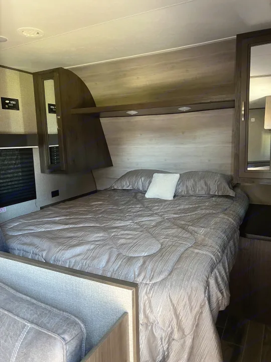 Comfortable RV rental bedroom with a full bed, gray bedding, built-in overhead storage, reading lights, and wall controls.. Jayco Jay Flight SLX Rocky Mountain Edition 2020