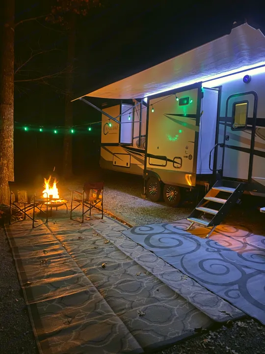 Cozy nighttime rv rental setup with a crackling campfire, outdoor rugs, and festive lights at a peaceful campsite.. Highland Ridge RV Open Range 2024