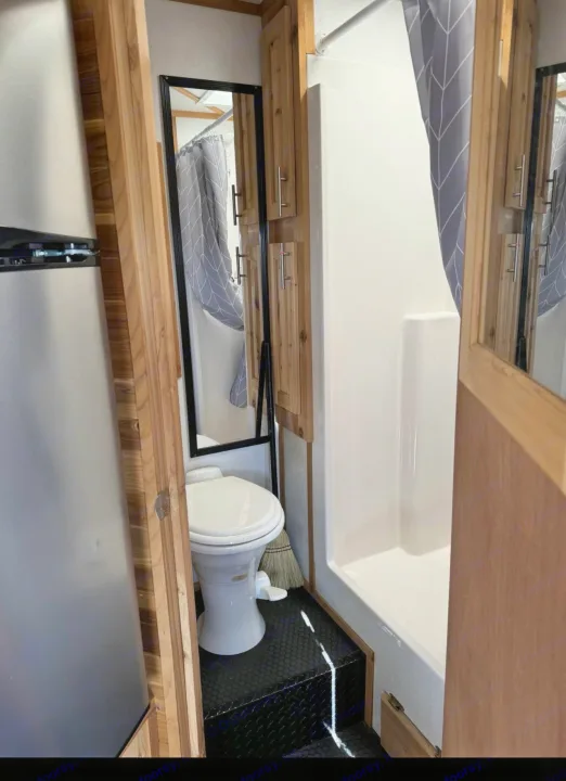 Compact RV rental interior: A bright bathroom with a white toilet, shower, and full-length mirror. Fridge on left.. Ice Castle Fish Houses Toy Hauler 2019