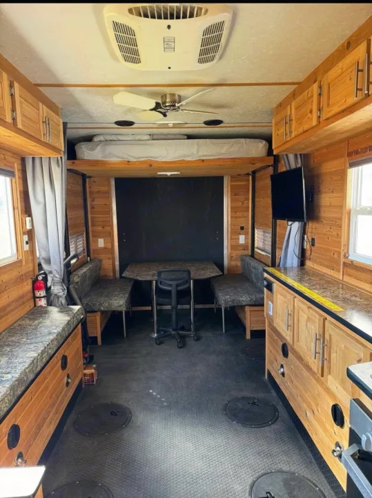 Spacious RV rental interior with rustic wood, overhead bed, kitchen, dining, and floor access for ice fishing.. Ice Castle Fish Houses Toy Hauler 2019