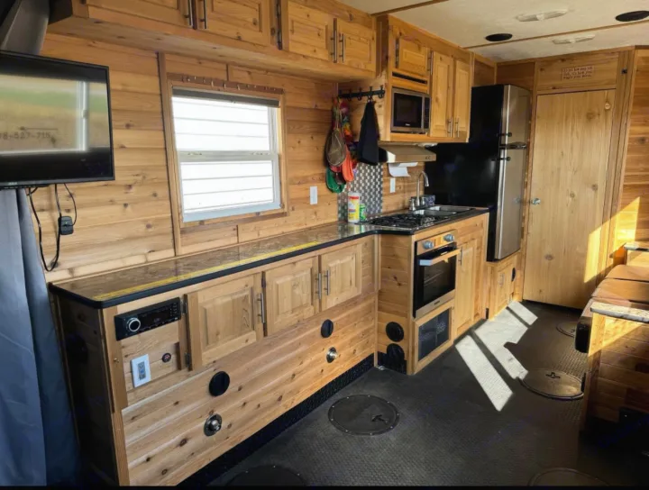 Cozy wood-paneled RV rental interior with full kitchen, TV, and floor hatches, ideal for ice fishing.. Ice Castle Fish Houses Toy Hauler 2019