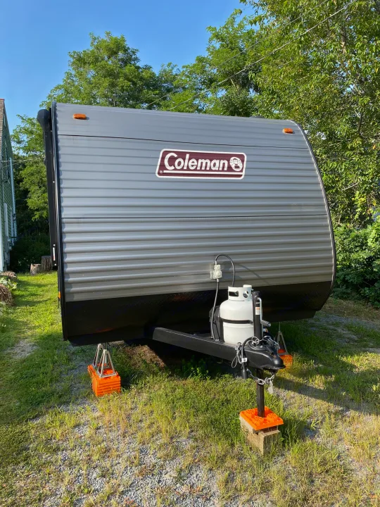 Coleman travel trailer RV rental, parked outdoors on grass with leveling blocks & propane tank.. Coleman Lantern 17B 2024