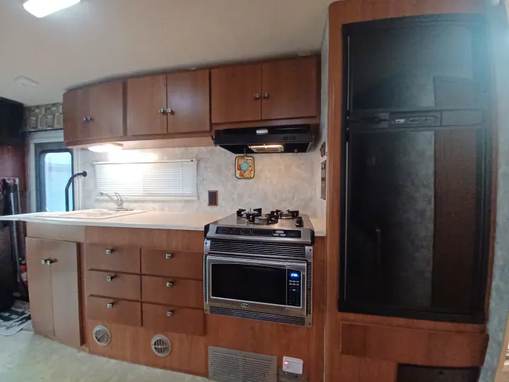 Inside an RV rental, a well-equipped kitchen features wooden cabinets, sink, microwave, stove, and a refrigerator.. Winnebago Outlook 2007
