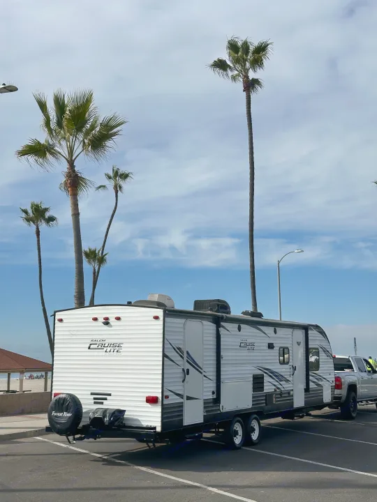 White Forest River Salem Cruise Lite rv rental trailer hitched to a truck, parked on a sunny day near a beach with palm trees.. Forest River Salem Cruise Lite 2019