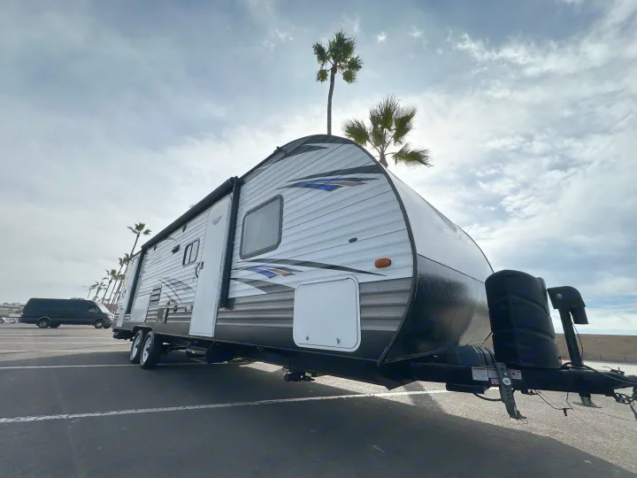 White & black travel trailer RV rental, parked under cloudy sky with palm trees. Dark van visible in background.. Forest River Salem Cruise Lite 2019