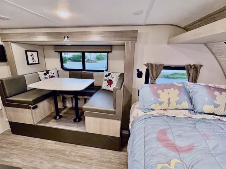 Cozy Disney-themed RV rental interior featuring a spacious dinette with Mickey pillows and a comfortable bed.. Forest river Aurora 2025
