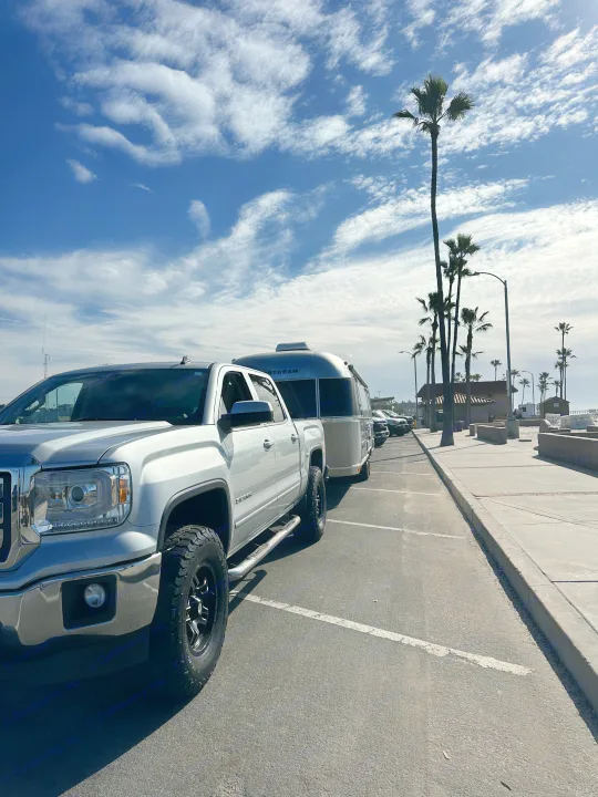 Silver pickup truck towing an Airstream RV in a sunny parking lot near palm trees. Consider an RV rental for your next trip!. Airstream Flying Cloud 2019