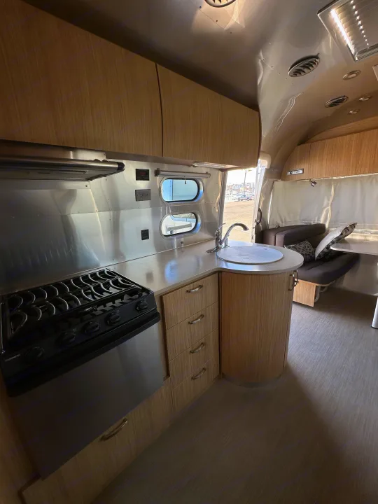 Spacious RV rental interior featuring a modern kitchen with stove, sink, and cabinets, plus a cozy dinette area.. Airstream Flying Cloud 2019