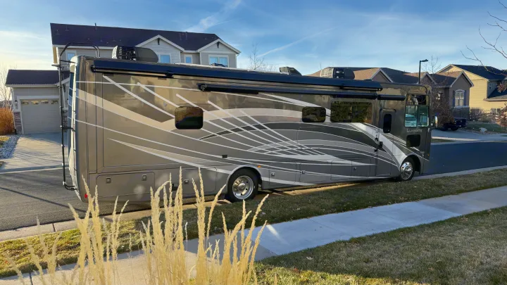 Modern gray Class A motorhome with bold side graphics, parked curbside on a sunny day. Perfect for your next RV rental adventure.. Thor Luminate 2024