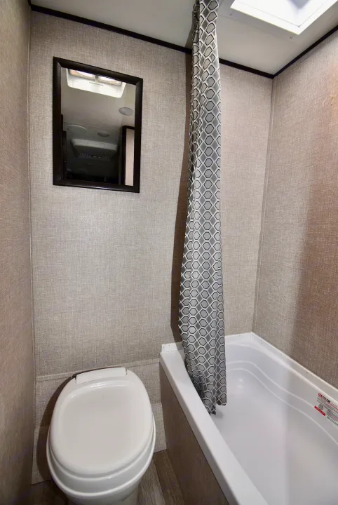 Compact RV rental bathroom with toilet, small tub/shower, mirror, textured walls, and geometric curtain.. Jayco Jay Flight SLX 2022