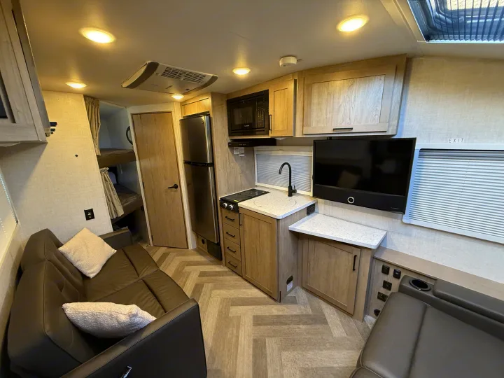 This RV rental interior showcases a full kitchen, living area with sofa, and rear bunk beds, ideal for travel.. Ember Overland 2023
