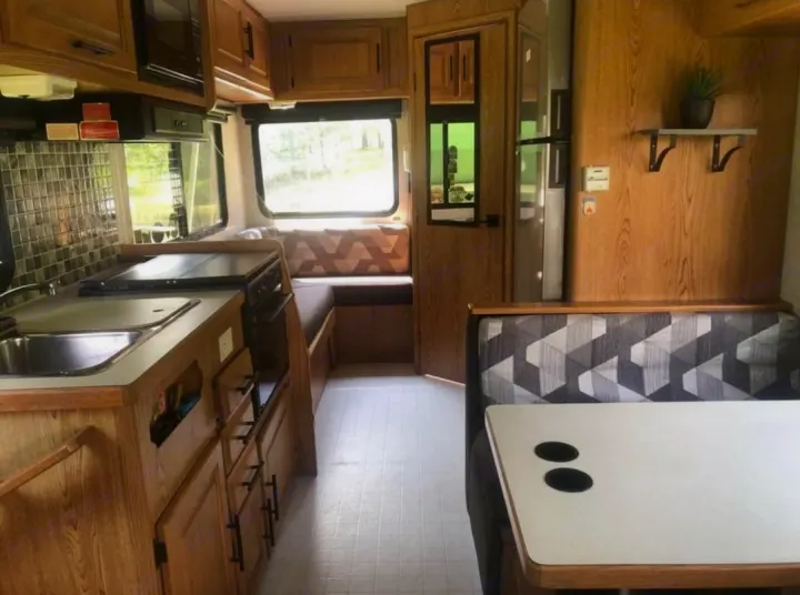 RV rental interior: compact kitchen (sink, stove, microwave), dinette with patterned cushions, fridge, and wood cabinetry.. Ford Ford E350 1996