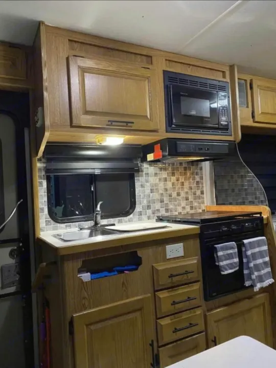 Interior of an RV rental kitchen showing wooden cabinets, sink, microwave, oven, and tiled backsplash.. Ford Ford E350 1996