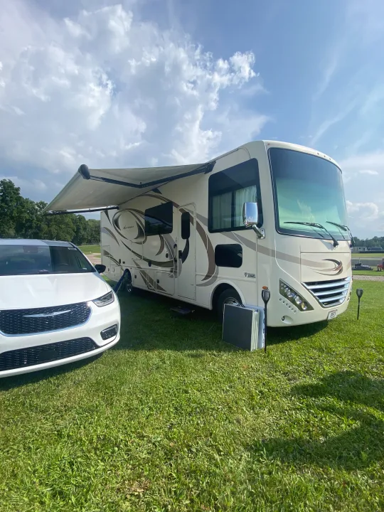 Thor Hurricane RV rental with an extended awning, parked on green grass next to a white minivan. Perfect for camping trips!. Thor Hurricane 2018