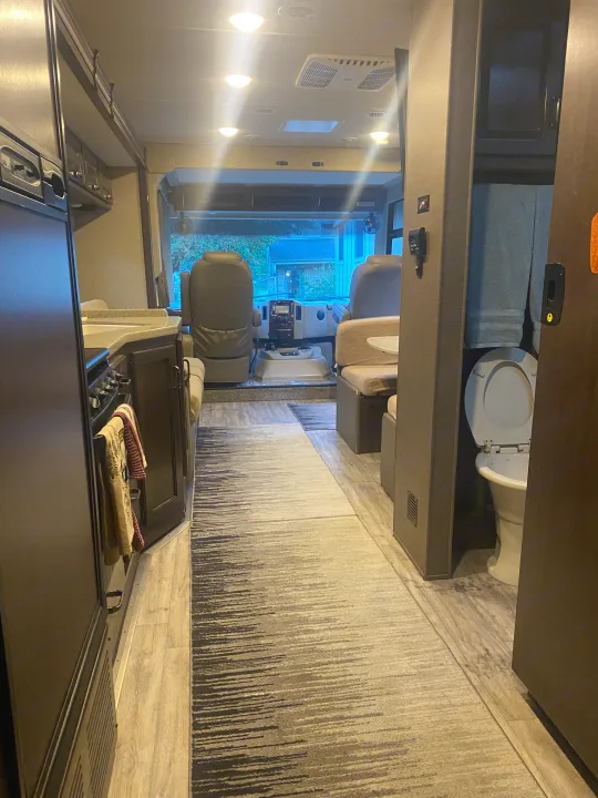 Interior of an RV rental: kitchen on left, cockpit forward, dining on right, and a glimpse of the bathroom with toilet.. Thor Hurricane 2018