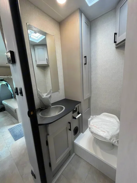 Modern RV rental bathroom with a compact design, featuring a sink, toilet, mirror, and light gray cabinets for travel comfort.. Forest River Coachmen Freelander 2026