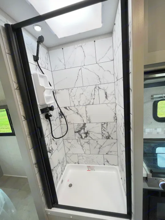 Modern RV rental shower featuring black trim, white marble-look tiles, white base, handheld showerhead, and bright overhead lighting.. Forest River Coachmen Freelander 2026