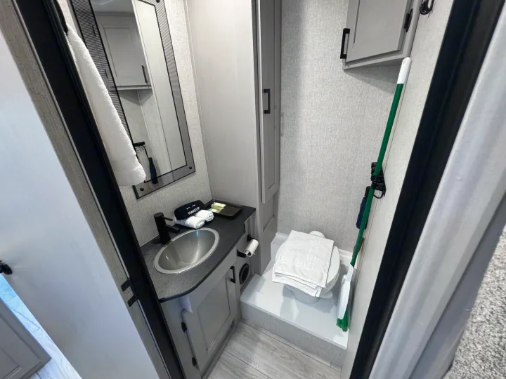 Experience comfort in this RV rental bathroom: sink, mirror, toilet with towels, and wall-mounted brush. Space-efficient design.. Forest River Coachmen Freelander 2026