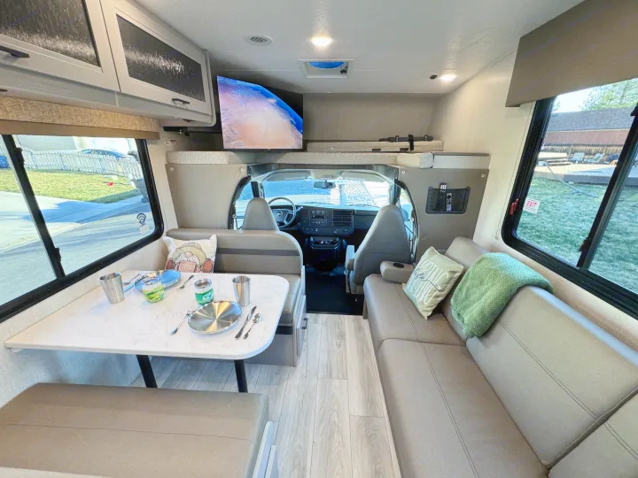 Bright rv rental interior: dining booth, sofa, overhead TV & bunk, plus the front cab area. Ready for your next adventure.. Forest River Coachmen Freelander 2026