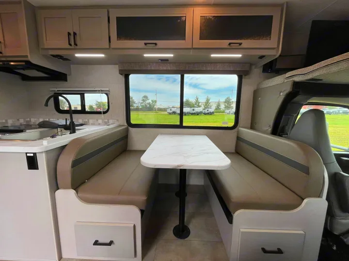 This RV rental interior features a cozy dinette, kitchenette, and overhead storage, ideal for travel adventures.. Forest River Coachmen Freelander 2026