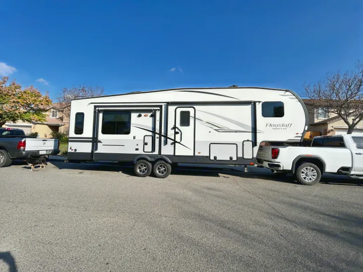 A large Flagstaff travel trailer RV rental, hitched to a white pickup truck, on a residential street with a dog.. Forest River Flagstaff Super Lite 2019