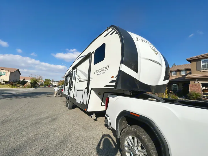 A white fifth-wheel RV, ideal for an RV rental adventure, is towed by a pickup truck on a sunny residential street.. Forest River Flagstaff Super Lite 2019
