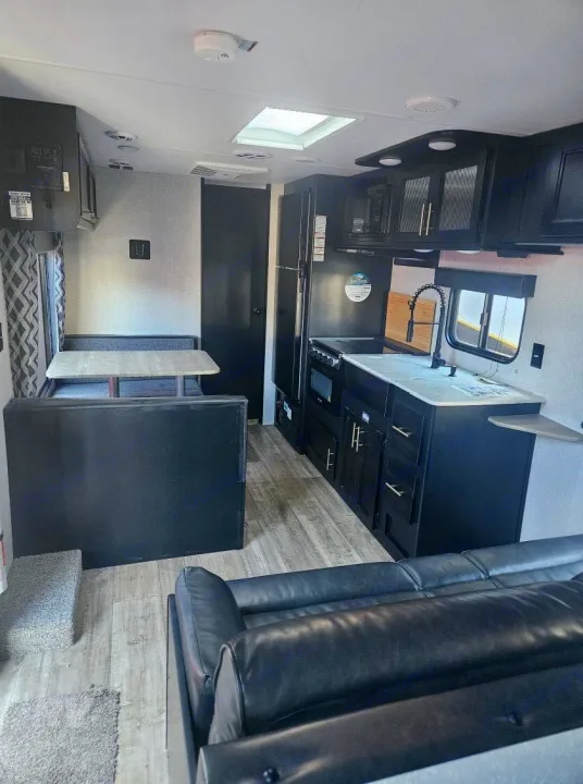 Modern rv rental interior featuring a sleek black kitchen, spacious dinette, and comfortable living area with a sofa.. Forest River Cherokee Grey Wolf 2022